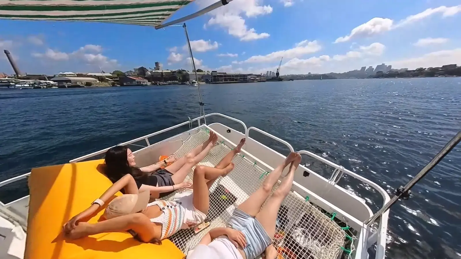 Two guests lying on the trampoline sunbed beside the yellow beanbag, Cockatoo Island's cranes behind