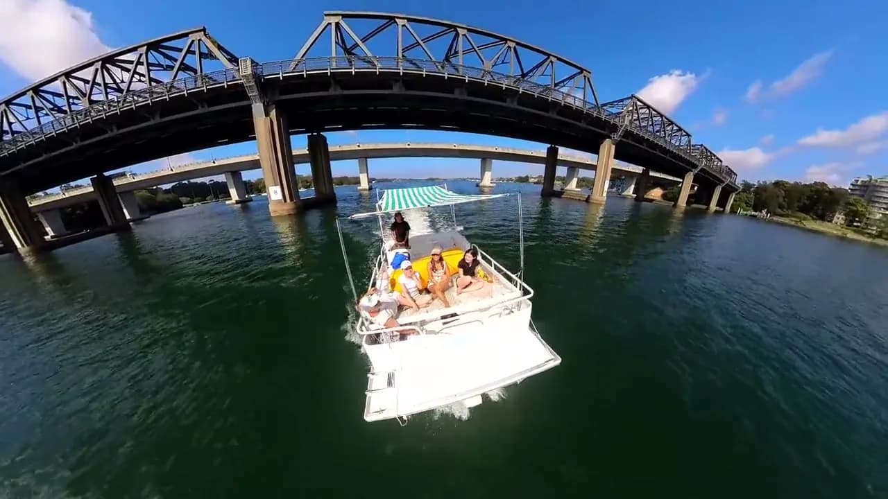Capri passing under the Iron Cove Bridge, striped canopy up, guests on the deck